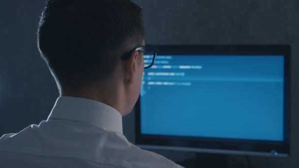 Vista posterior del programador profesional en gafas código de programación en el monitor de la computadora en la oficina nocturna — Vídeos de Stock