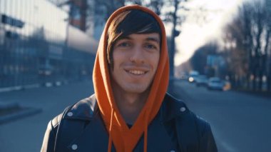 Sırt çantaları olan yakışıklı genç adam kameraya bakıyor ve gülümsüyor. Gün batımı kentsel arka planda kameraya bakarak rahat giysiler giyen yakışıklı beyaz adam