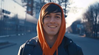 Sırt çantaları olan yakışıklı genç adam kameraya bakıyor ve gülümsüyor. Gün batımı kentsel arka planda kameraya bakarak rahat giysiler giyen yakışıklı beyaz adam