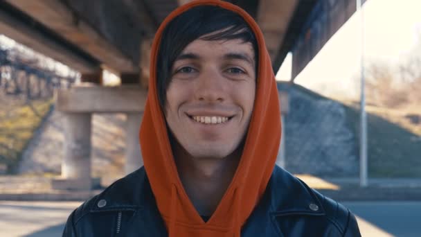 Retrato de homem caucasiano feliz com capuz vermelho sorrindo na cidade no fundo urbano — Vídeo de Stock