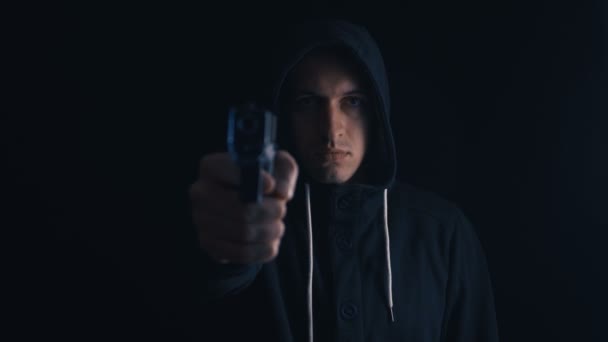 危険なフード付き犯罪者は黒い背景に彼の銃を目指しています — ストック動画