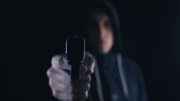 Farliga Hooded kriminella mål hans pistol på svart bakgrund. Fokus ligger på pipan med en hand pistolgrepp. — Stockvideo