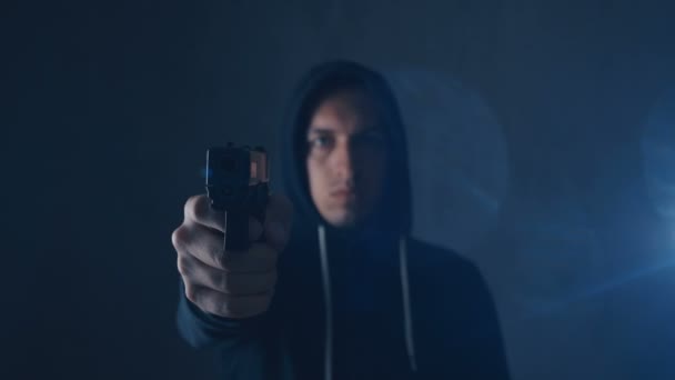 Gefährlicher Kapuzen-Verbrecher zielt mit Waffe auf schwarzen Hintergrund — Stockvideo