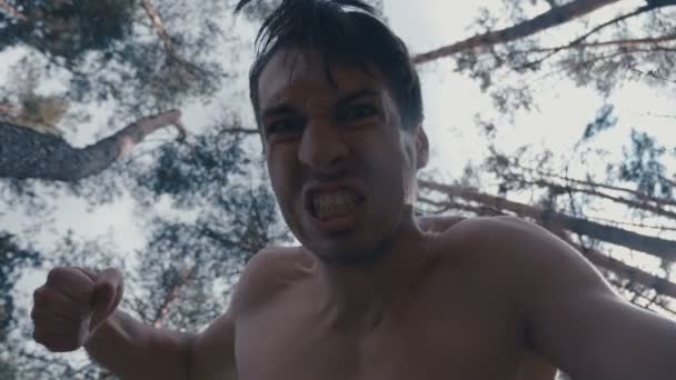 Яростный агрессивный человек бьет кулаками лежащего в лесу человека — стоковое видео