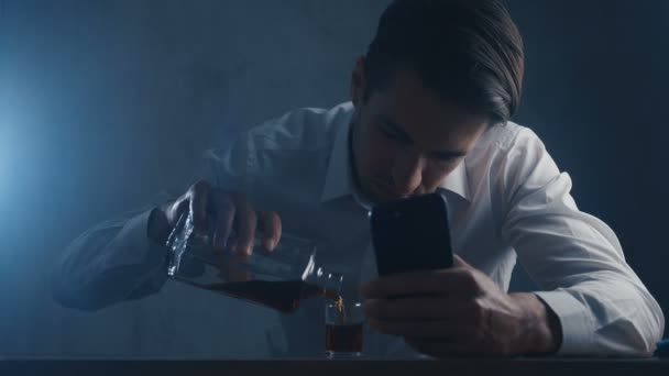 Un empresario deprimido vierte whisky en un vaso de chupito bebiendo solo en una habitación oscura. Concepto de alcoholismo . — Vídeo de stock