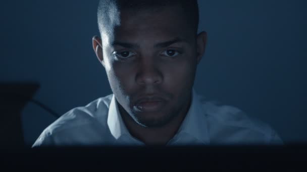 Close-up van een jonge en drukke Afrikaanse zakenman die 's nachts op de computer werkt. — Stockvideo