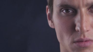 Yarım yüz portre konsantre genç adamın gözleri açılır ve kamera için siyah arka plan üzerine görünüyor