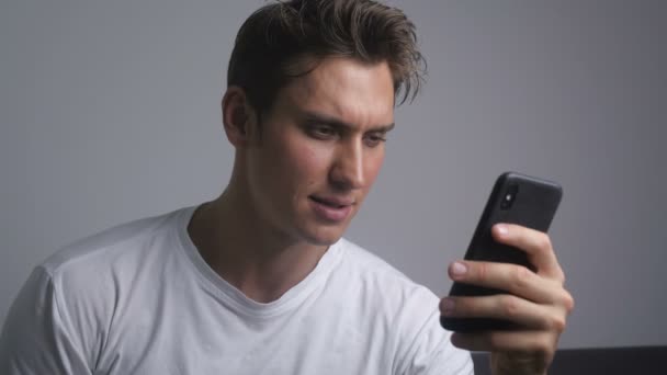 Hombre sonriente atractivo usando smartphone enviando mensaje en las redes sociales y bebiendo café en interiores — Vídeos de Stock