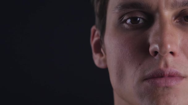 Полупортрет концентрированного молодого человека открывает глаза и смотрит в камеру на черном фоне — стоковое видео