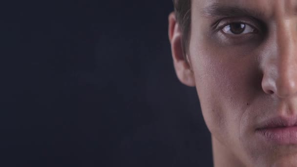 Half face portrait of concentrated young man opens his eyes and looks to camera on black background — Stock Video