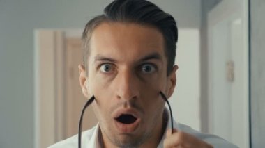 Genç adamın portresi şaşırır ve şok içinde gözlüklerini çıkarır. Görme konusunda endişeli.