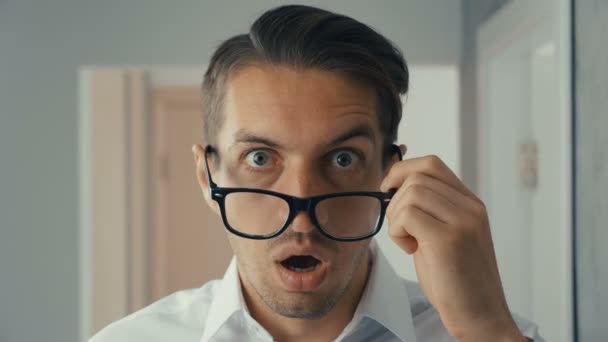 Porträtt av ung man är förvånad och lyfter hans glasögon i chock. Han är orolig för att se — Stockvideo