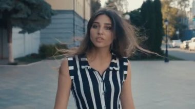 Genç ve güzel bir kadın şehirde yürüyor, dönüyor ve gülümsüyor. Kamera arkadan takip et.