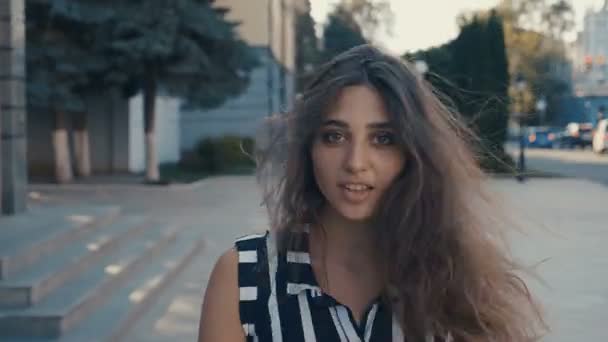 Fiatal, gyönyörű nő sétál, fordul és mosolyog a városban. Kamera kövesse mögötte. — Stock videók