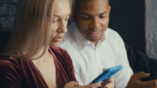 카페 나 사무실 배경에서 스마트 폰을 사용하는 혼합 인종 커플. 남녀가 스마트폰을 통신하고 사용 — 비디오