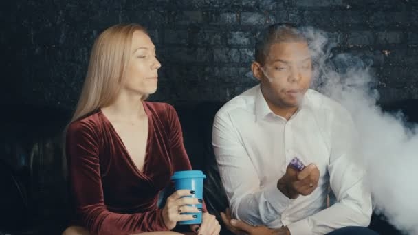 Pareja multiracial hablando en cafetería, hombre fumando vapor y mujer tomando café en restauracióntía, diversas personas negociando en reunión en cafetería — Vídeos de Stock