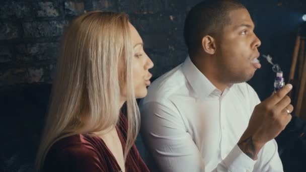 Pareja multiracial hablando en cafetería, hombre fumando vapor y mujer tomando café en restauracióntía, diversas personas negociando en reunión en cafetería — Vídeo de stock