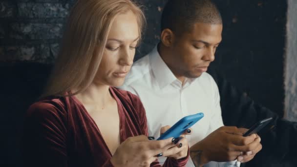 Mixed race couple using smartphone in cafe or office background. Man and woman communicate and use smartphones — Stock Video