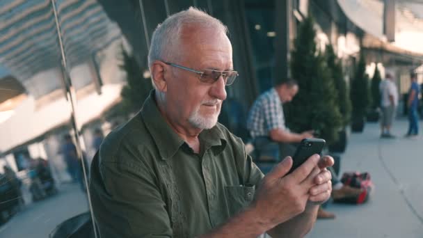 Senior man met smartphone buitenshuis op Airport Terminal — Stockvideo