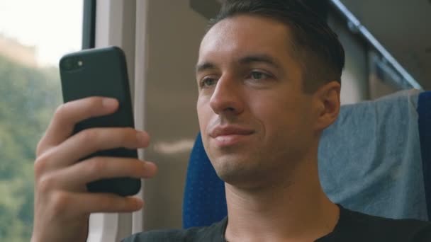 Молодой человек использует свой смартфон, записывает и прокручивает во время поездки на поезде — стоковое видео