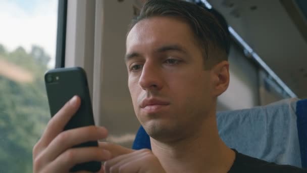 Молодой человек использует свой смартфон, записывает и прокручивает во время поездки на поезде — стоковое видео