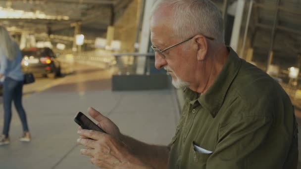 空港ターミナルで屋外でスマホを使うシニア男性 — ストック動画