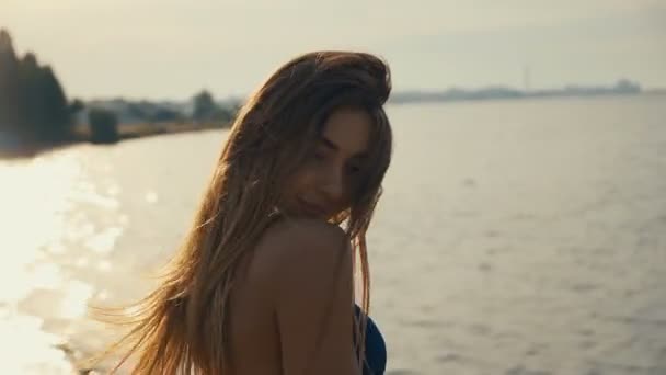 Retrato de una joven seductora con el pelo largo en bikini posando al atardecer en la playa — Vídeos de Stock