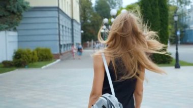 Çekici uzun saçlı woung kadın şehir-sokakta yürürken geri görünümü, kameraya döner ve güzel bir gülümseme verir, rüzgar saçları ile oynar. Steadicam atış.