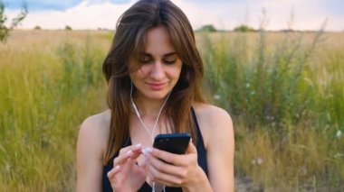 Mutlu genç kadın gün batımında sahada duran akıllı telefon ve kulaklık kullanın, sağlıklı yaşam tarzı. Akıllı telefon açık kullanarak Sportywoman koşucu.