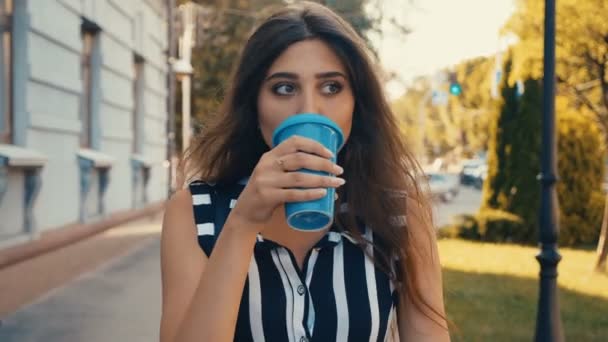 Framsidan av ung vacker kvinna dricka kaffe medan du går ner i centrum. — Stockvideo