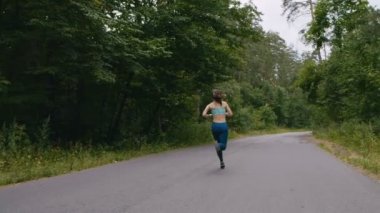 Koşucu kadın yavaş hareket halinde ormanda yolda koşuyor. açık fitness. Steadicam ile vuruldu. Sabah çalışan kavramı.