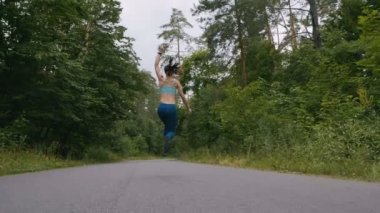 Koşucu kadın koşuyor ve ormanda yavaş hareketle yola atlıyor. açık fitness. Steadicam ile çekim.