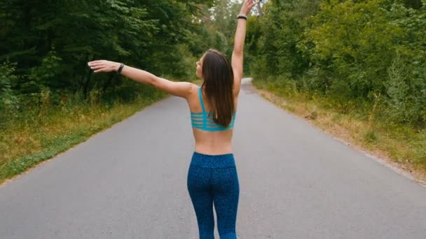 女运动员慢跑者在森林道路上行走时举手，享受自由，相信未来会成功。自信的神志女性享受在公园醒来，成就和灵感. — 图库视频影像