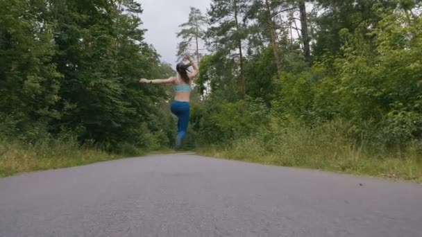 Koşucu kadın koşuyor ve ormanda yavaş hareketle yola atlıyor. açık fitness. Steadicam ile çekim. — Stok video