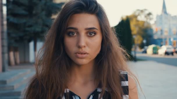 Retrato de cerca de la hermosa modelo morena mujer joven mirando a la cámara en un fondo de calle de la ciudad. Chica con grandes ojos . — Vídeos de Stock