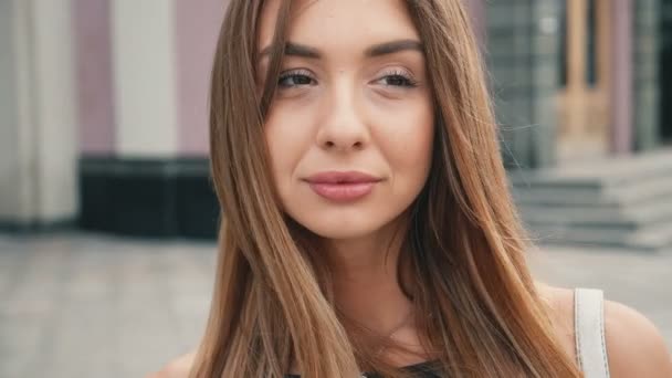 Cara de cabello castaño claro joven mujer mirando cámara steadicam disparo. Retrato hermosa mujer en la ciudad urbana calle fondo . — Vídeo de stock