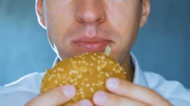 Adam bir hamburger yiyor, yakın çekim. Hızlı yemek. Cheeseburger, hamburger, sandviç.