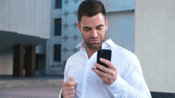 Empresario Celebrando el éxito mientras lee el mensaje en el teléfono inteligente cerca del edificio de oficinas. Guapo profesional exitoso hombre de negocios alcanzando objetivos personales . — Vídeos de Stock