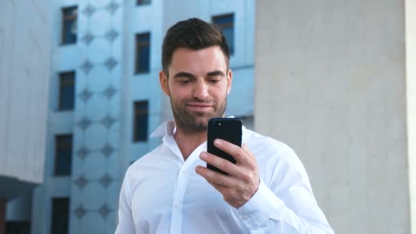 Zakenman viert succes tijdens het lezen van bericht in smartphone in de buurt van kantoorgebouw. Knappe professionele succesvolle zakelijke man het bereiken van persoonlijke doelen. — Stockvideo