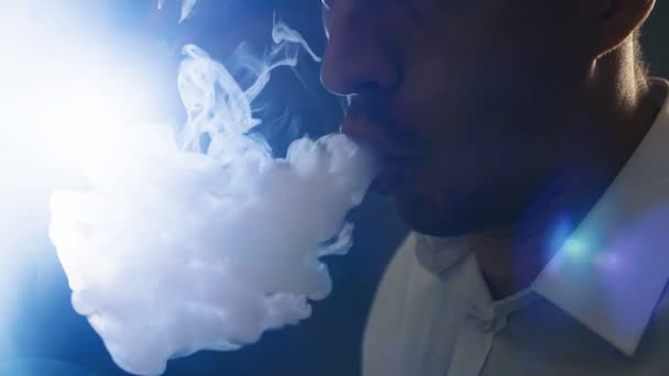 Крупный план бизнесмена, испаряющего электронную сигарету в темной комнате — стоковое видео