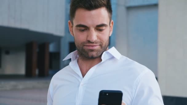 Empresario Celebrando el éxito mientras lee el mensaje en el teléfono inteligente cerca del edificio de oficinas. Guapo profesional exitoso hombre de negocios alcanzando objetivos personales . — Vídeo de stock