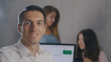 Arka planda insanlar ekibi ile ofiste gülümseyen yüzü ile genç erkek takım lideri Portresi. Profesyonel yönetici işadamı.