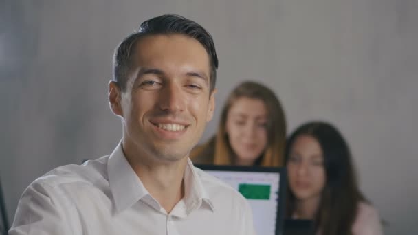 Retrato del joven líder del equipo masculino con la cara sonriente en la oficina con el equipo de personas en el fondo. Gerente profesional hombre de negocios . — Vídeos de Stock