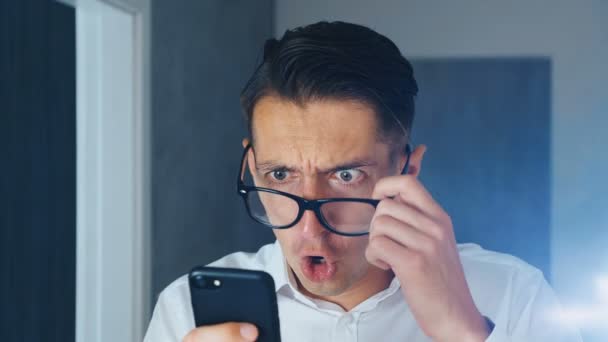 Retrato de homem chocado e enojado. O homem confuso viu uma mensagem desagradável em um smartphone, de surpresa adia óculos e olha para a câmera. Ele está preocupado em ver. Close-up . — Vídeo de Stock