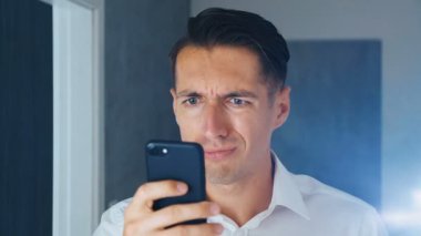 Şok edilmiş ve iğrenmiş bir adamın portresi. Kafası karışmış bir adam akıllı telefonda tatsız bir mesaj görmüş. Görmekten korkuyor. Close.