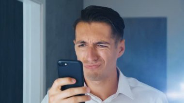 Şok edilmiş ve iğrenmiş bir adamın portresi. Kafası karışmış bir adam akıllı telefonda tatsız bir mesaj görmüş. Görmekten korkuyor. Close.