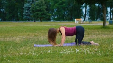Genç beyaz kadın sabah ları açık hava yerinde yoga yaparak dinlendiriyor. Güzel kadın yeşil çim parkta yoga yapıyor