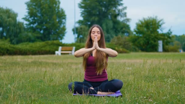 Mulher bonita jovem meditando durante o treinamento ao ar livre no parque de verão ela sentindo paz. Menina desportiva fazendo ioga ao ar livre pela manhã . — Vídeo de Stock