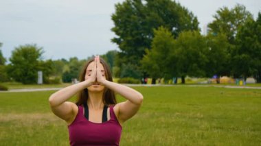 Genç beyaz kadın sabah ları açık hava yerinde yoga yaparak dinlendiriyor. Güzel kadın yeşil çim parkta yoga yapıyor