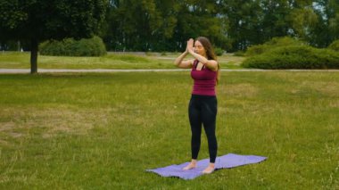 Genç beyaz kadın sabah ları açık hava yerinde yoga yaparak dinlendiriyor. Güzel kadın yeşil çim parkta yoga yapıyor